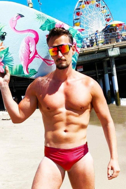 Man holding surfboard wearing red swim briefs