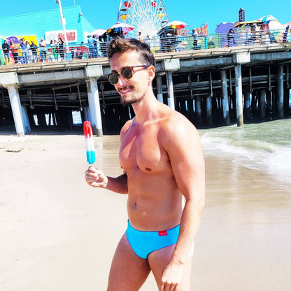 Man wearing turquoise swim briefs on beach