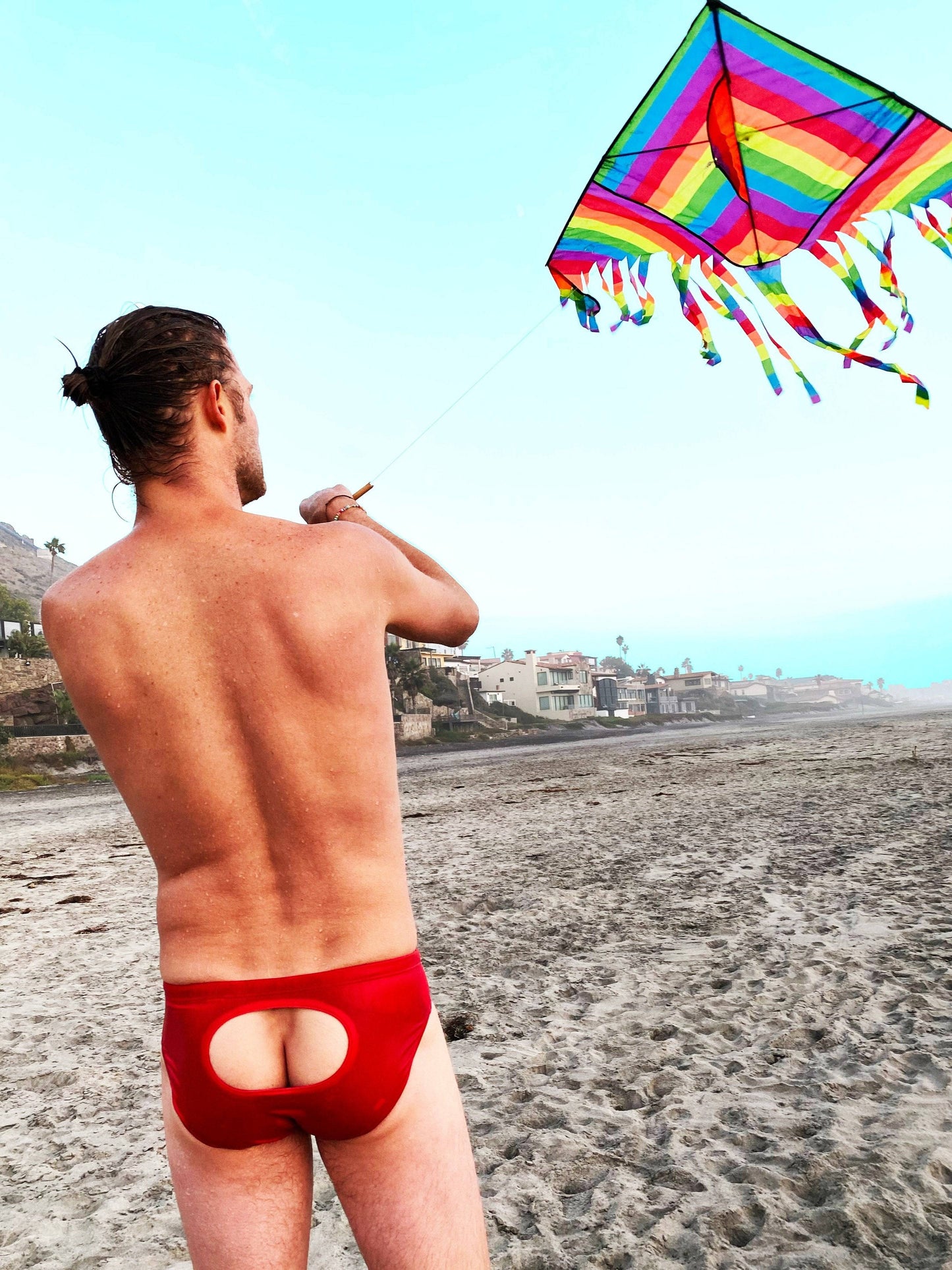 Man on beach flying kite in red open window swim briefs